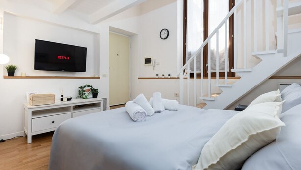 A hotel room with a bed, a TV mounted on the wall, a staircase, and a clock. - Cozy 45m2 apartment, ideal for 4 people, located on the ground floor of a building.The accommodation is located in a residential area 2 steps from the famous Prada Foundation, center of culture and fashion, and a short distance from the Milano Porta Rom (Milan)