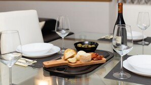 A dining table with a bottle of wine, glasses, a bowl of olives, and a wooden board with bread and cheese. - Cozy 45m2 apartment, ideal for 4 people, located on the ground floor of a building.The accommodation is located in a residential area 2 steps from the famous Prada Foundation, center of culture and fashion, and a short distance from the Milano Porta Rom (Milan)