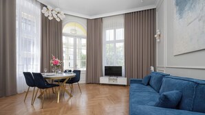 Een moderne woonkamer met een blauwe bank, een houten eettafel en een televisie op een witte kast.
