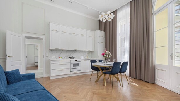 Een moderne keuken met witte kastjes, een eethoek met een tafel en stoelen, en een blauwe bank.