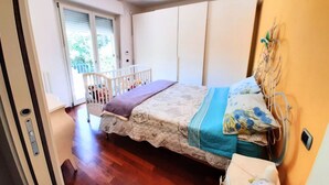 Un dormitorio con cama, cuna y puerta corrediza a un balcón.