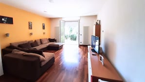 Un salón con sofá modular, televisor de pantalla plana y puerta corrediza de vidrio que da a un balcón.