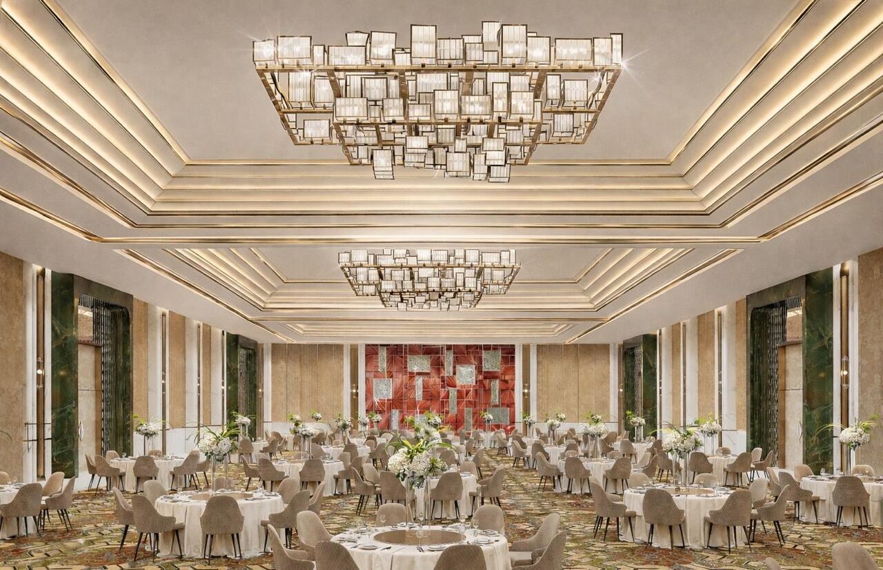 A spacious banquet hall with round tables, a large chandelier, and a patterned carpet.
