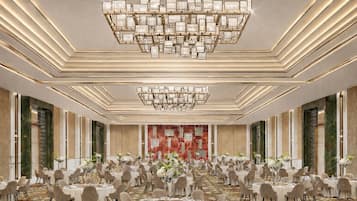 A spacious banquet hall with round tables, a large chandelier, and a patterned carpet.