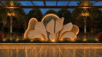 A water feature with leaf-shaped structures and a central fountain, surrounded by palm trees and greenery.