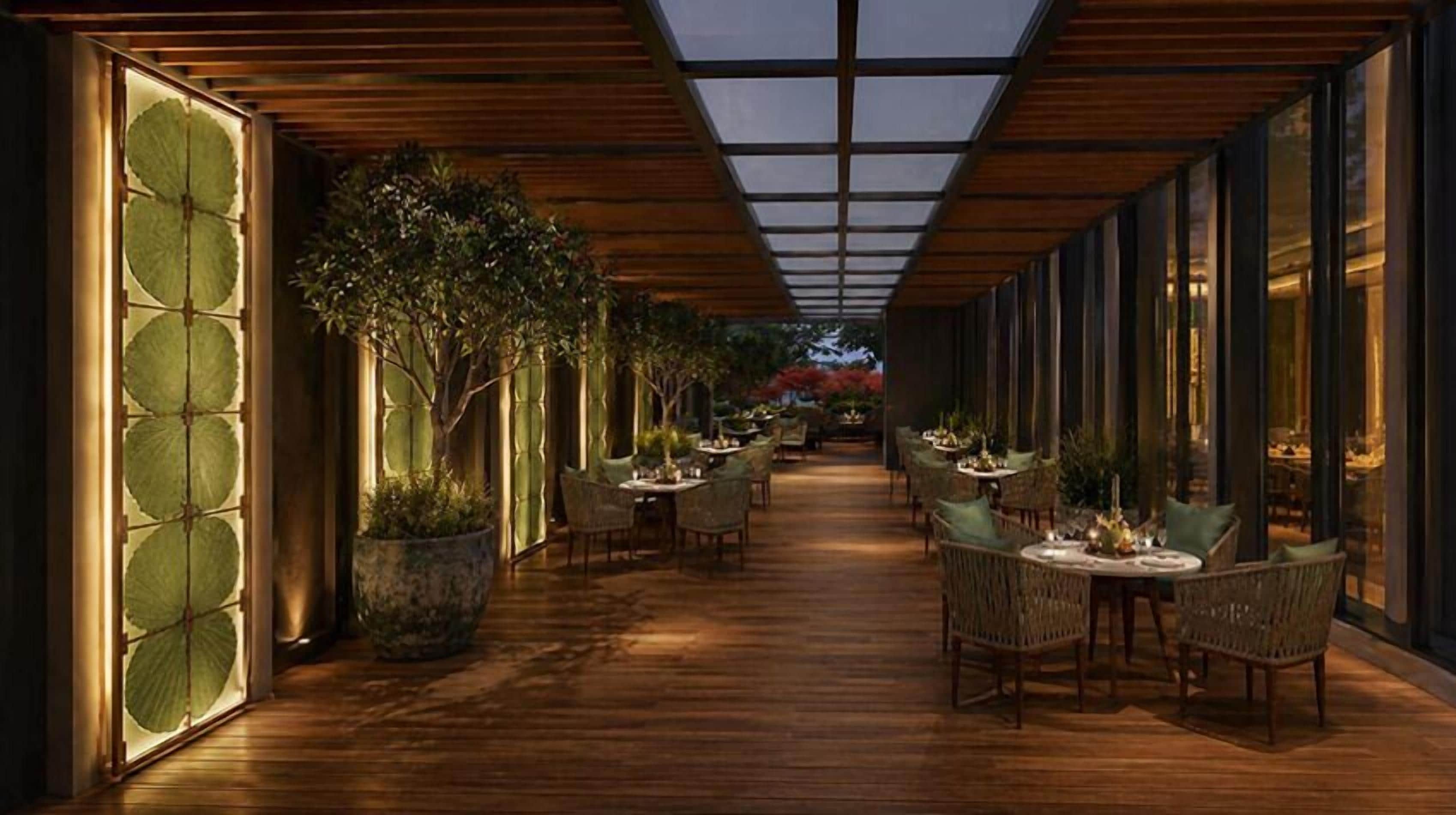 A corridor with tables and chairs, large windows, and potted plants.