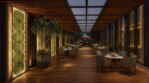 A corridor with tables and chairs, large windows, and potted plants. - Altara Indore (Indore)