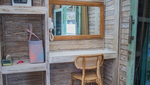 Una habitación rústica de madera con una repisa que sostiene un bolso estampado, una silla de mimbre y un espejo que refleja una puerta.