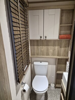 A bathroom with a toilet, a roll of toilet paper, a towel, and a window with blinds.