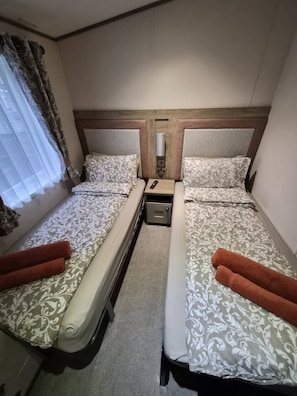 A hotel room with two beds, each with patterned bedding and a remote control on the nightstand.