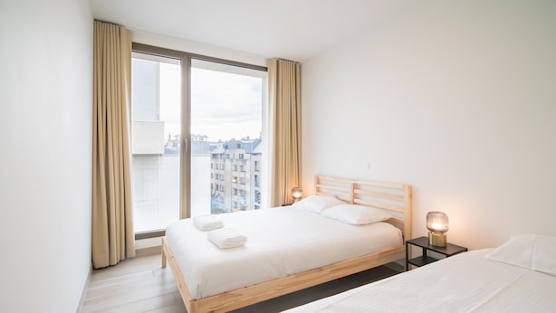 Ein Hotelzimmer mit großem Fenster, einem hölzernen Bett, einem Nachttisch mit Lampe und einem weiteren Bett.