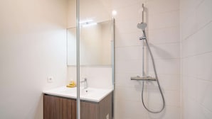 Ein modernes Badezimmer mit einer Duschkabine aus Glas, einem weißen Waschbecken und einem Holzkabinet.