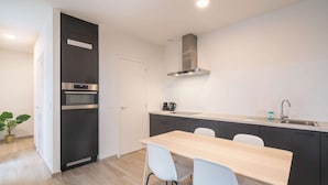 Eine moderne Küche mit Einbauofen, Dunstabzugshaube aus Edelstahl, Spüle und Essbereich mit Tisch und Stühlen.