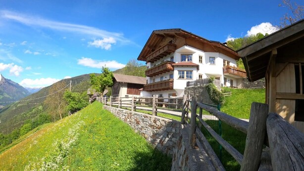 Un chalet traditionnel, doté d’un mur en pierre et d’une clôture en bois, situé dans une région montagneuse où le ciel est dégagé.