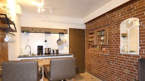 Uma cozinha moderna com parede de tijolos, uma área de refeições com duas cadeiras e uma estante embutida com utensílios de cozinha.