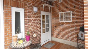 Fachada de tijolos com um pátio ladrilhado, uma porta branca e uma pequena mesa com plantas em vasos.