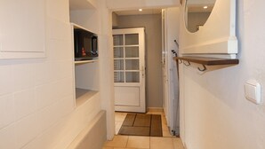 Um corredor estreito com paredes brancas, um micro-ondas numa prateleira, uma porta que dá para outro quarto e um espelho na parede.