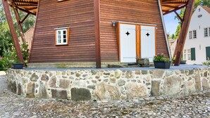 Maalaishenkinen puutalo, jossa on kivinen perustus, pieni ikkuna ja tähtiä kuvaavilla koristeilla varustettu ovi.