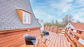 A wooden deck with two chairs and a table, a window, and a sloped roof. - fewo1846 - Westwind - Vacation in a historic windmill with max. 4 persons (Flensburg)