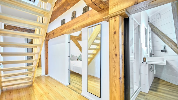 A room with wooden beams, a bed, a mirror, and a bathroom with a sink. - fewo1846 - Westwind - Vacation in a historic windmill with max. 4 persons (Flensburg)