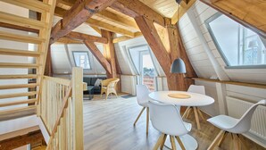 A loft-style room with exposed wooden beams, a dining table with chairs, and a sofa. - fewo1846 - Westwind - Vacation in a historic windmill with max. 4 persons (Flensburg)