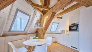 A modern kitchen with white cabinets, a built-in oven, and a dining area with a round table and white chairs. - Apartment 1846 - Ostwind - Vacation in a historic windmill for up to 4 people (Flensburg)