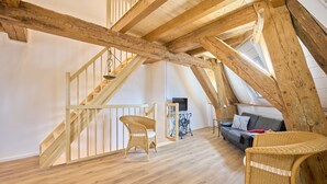 A loft-style room with exposed wooden beams, a wooden staircase, wicker furniture, and a black leather sofa. - Apartment 1846 - Ostwind - Vacation in a historic windmill for up to 4 people (Flensburg)