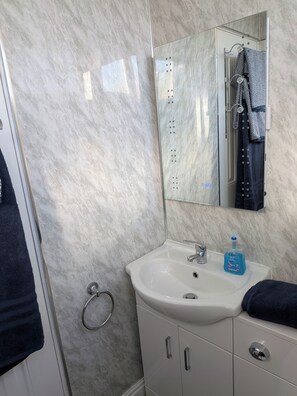 A bathroom with a marble wall, a sink with a mirror above it, and a towel rack with a towel. - Bungalow Sleeps 4 With Parking (Skegness)