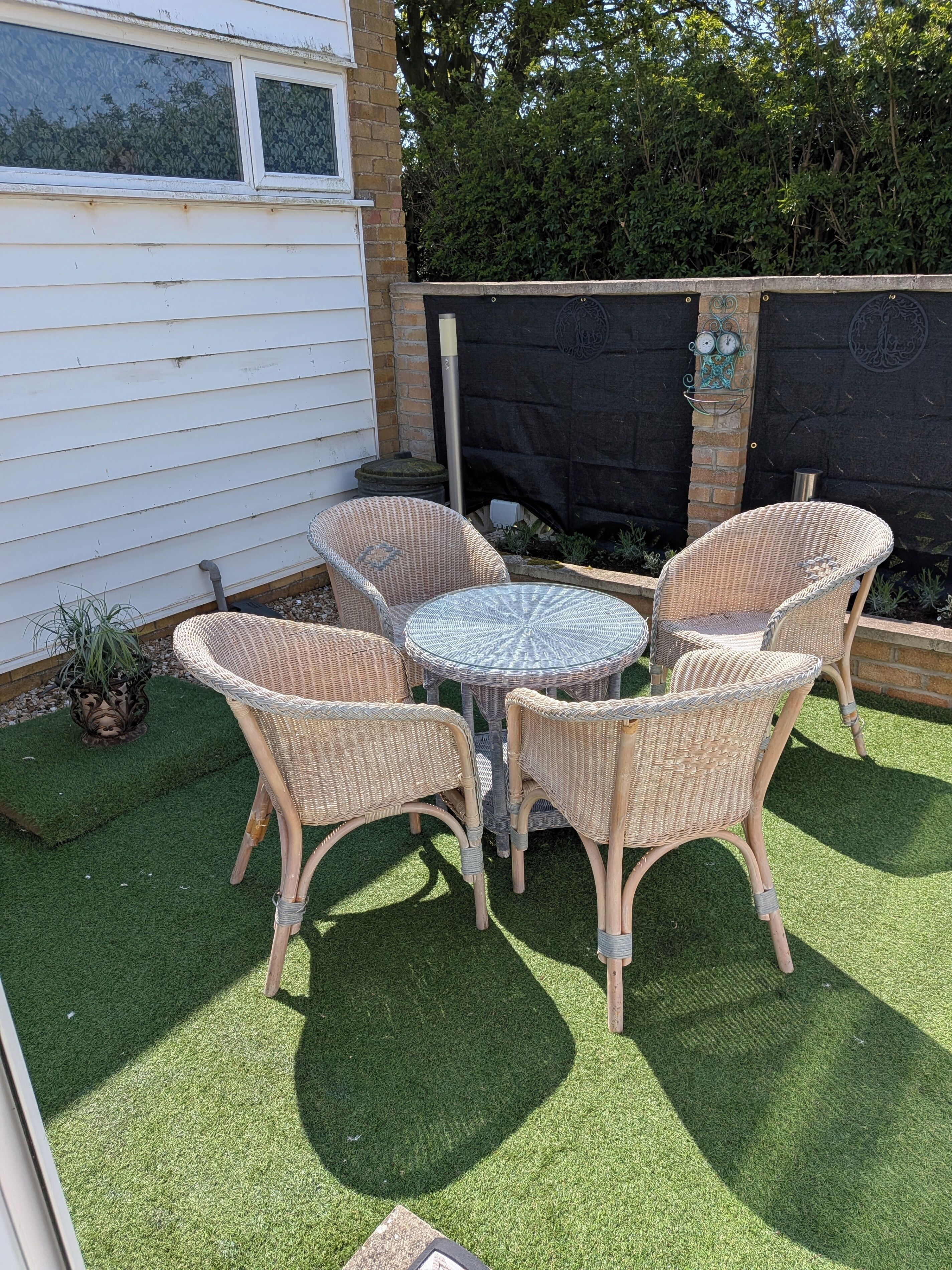 A patio with wicker furniture and a round table, surrounded by artificial grass.