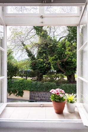 A window with a view of a tree-lined street and a potted plant on the windowsill. - Riverside 2BR Apartment Next to the National Theatre by EasyBNB Premium (Prague)