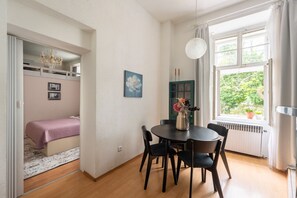 Et værelse med en seng, et spisebord med stole, en vase med blomster, en grøn dør og et vindue med udsigt over grønne områder.