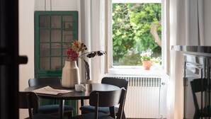 A dining area with a table, chairs, a vase with flowers, a green cabinet, and a window with a view of greenery. - Riverside 2BR Apartment Next to the National Theatre by EasyBNB Premium (Prague)