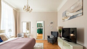 A modern hotel room with a large bed, a TV, a chair, a desk, and a view into the kitchen. - Riverside 2BR Apartment Next to the National Theatre by EasyBNB Premium (Prague)