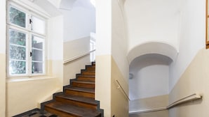 A staircase with wooden steps and a checkered floor, leading to a landing with a white wall and a window. - Riverside 2BR Apartment Next to the National Theatre by EasyBNB Premium (Prague)