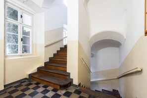 Eine Treppe mit Holzboden und Schachbrettmuster führt zu einer Zwischenebene mit weißer Wand und einem Fenster.