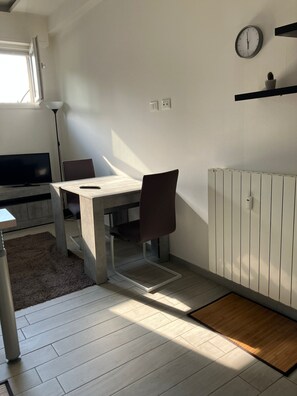 A modern room with a dining table, a single chair, a TV, a radiator, and a clock on the wall. - Vacation House in Bologna area Santa Viola Minisuite Reno (Bologna)