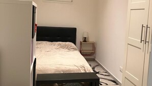 Une chambre à coucher de taille réduite, comprenant un lit, une armoire, une petite table avec une lampe et une fenêtre.