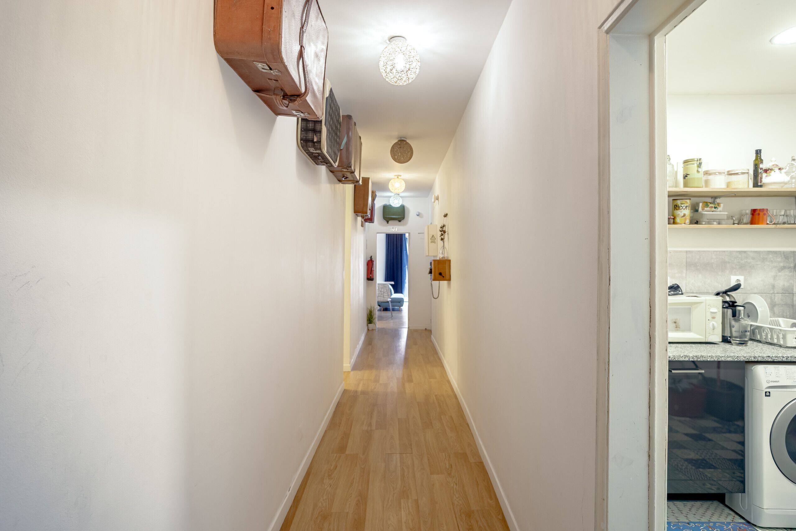 Un pasillo estrecho con suelo de madera, un ventilador de techo y una lavadora al fondo.