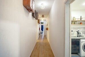 Ein schmaler Korridor mit Holzboden, Deckenventilator und einer Waschmaschine im Hintergrund.