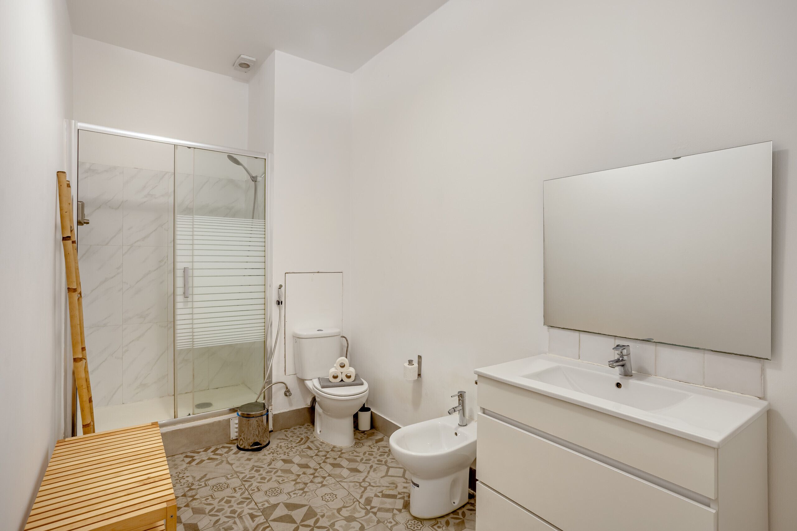 A bathroom with a shower, toilet, bidet, sink, and mirror.
