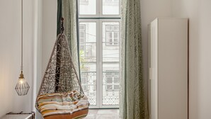 Ein Zimmer mit Hängesessel, Koffer, einer Lampe und Blick durch ein Fenster mit einer Tür.