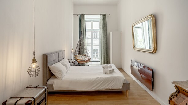 Ein Schlafzimmer mit Bett, Nachttisch, Hängesessel und einem großen Spiegel an der Wand.