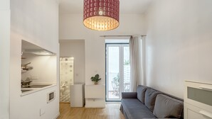 Eine moderne Küche mit Einbauofen, ein Essbereich mit Tisch und Stühlen, ein graues Sofa und ein großes Fenster mit Blick ins Freie.