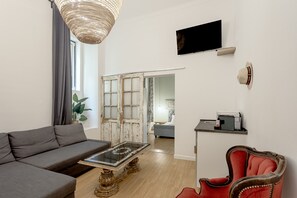 Ein modernes Wohnzimmer mit einer Couch, einem Glastisch, einem roten Sessel, einem Fernseher und einer Schiebetür zu einem anderen Raum.