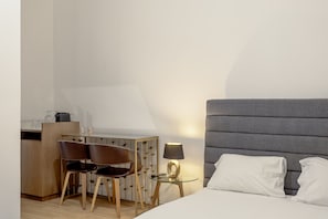 A hotel room with a bed, two chairs, a small table with a lamp, and a kitchenette area. - Boavista 130 Studios I by Homing (Lisbon)