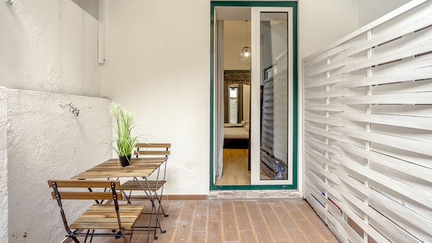 A narrow hallway with a wooden table and chairs, a potted plant, and a white wall with a green-framed door leading to another room. - Boavista 130 Studios I by Homing (Lisbon)