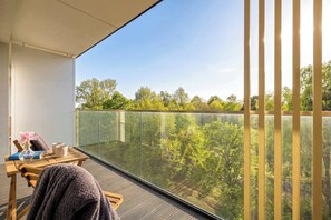 Een balkon met glazen hekwerk, een houten tafel en een stoel.