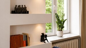 A modern living room with built-in shelves, a radiator, a potted plant, and a blue sofa. - Lumina Apart near Museum Fryderyk Chopin (Warsaw)