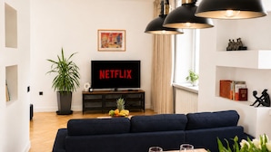 A modern living room with a dark blue sofa, a flat-screen TV, a potted plant, and a small table with glasses. - Lumina Apart near Museum Fryderyk Chopin (Warsaw)