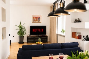 Ein modernes Wohnzimmer mit einem dunkelblauen Sofa, einem Flachbildfernseher, einer Topfpflanze und einem kleinen Tisch mit Gläsern.